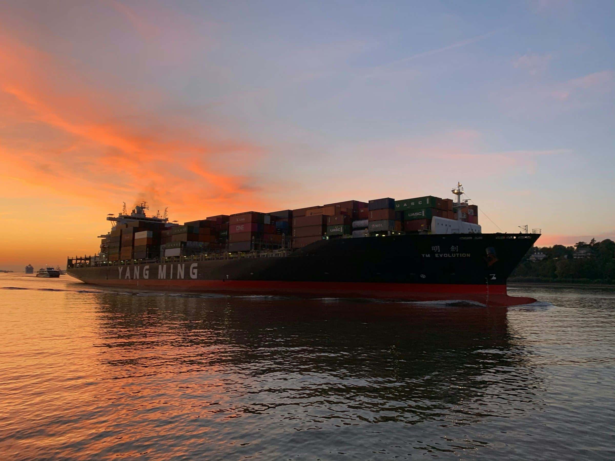 Container ship sailing at sunset under an orange sky