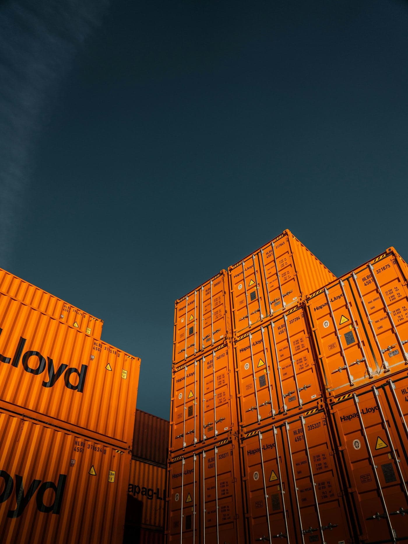 Stacked orange shipping containers against a deep blue sky