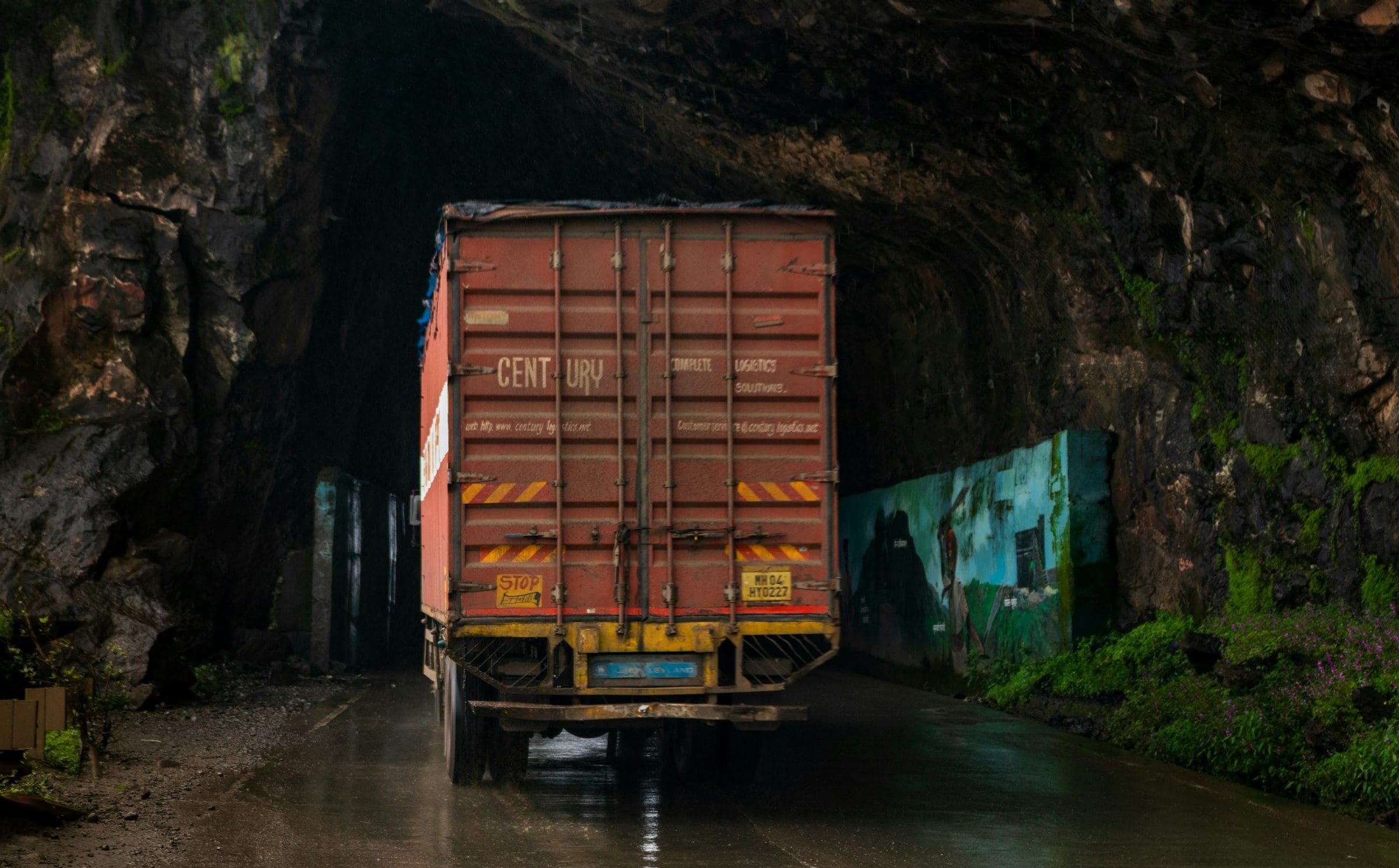 Container truck driving through a rock-cut tunnel on a wet Indian ghat road